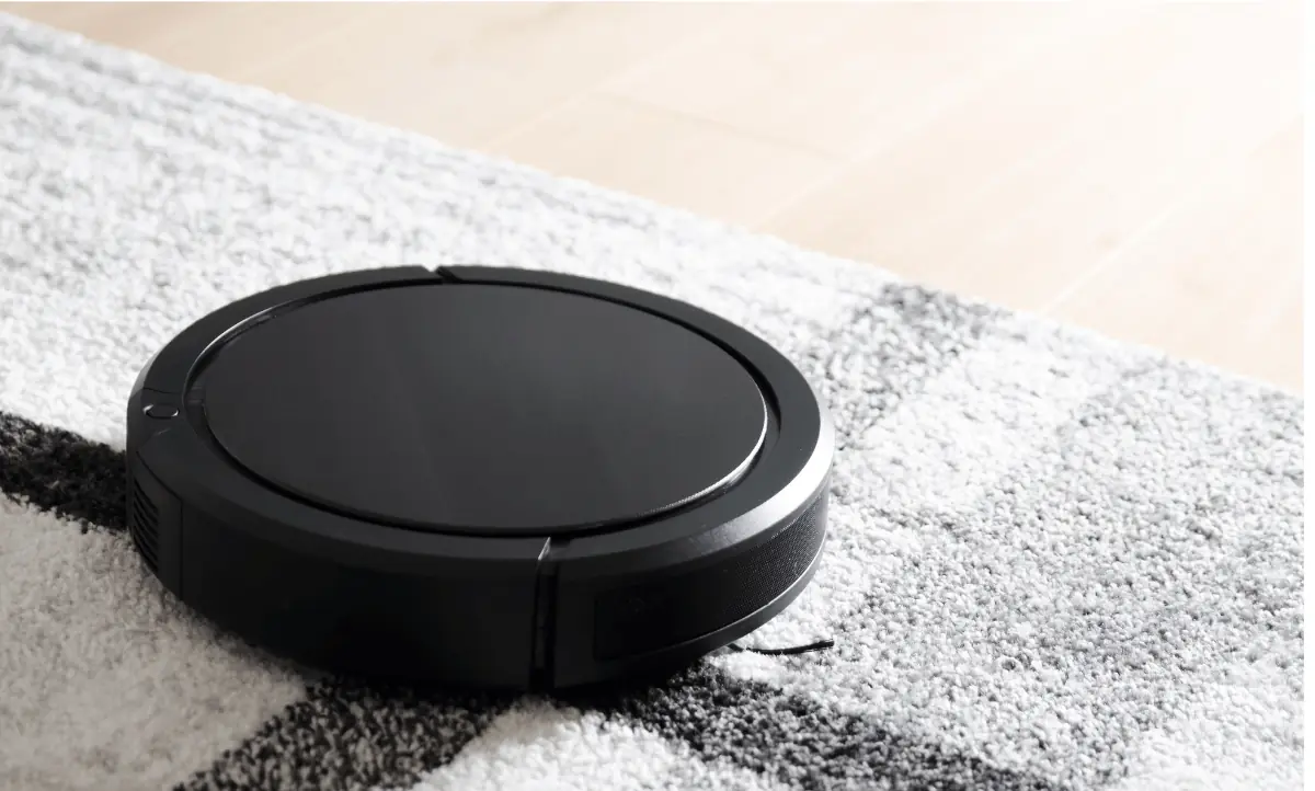 Slimme technologie in huis zoals deze zwarte robotstofzuiger schoonmakend op een grijs tapijt.