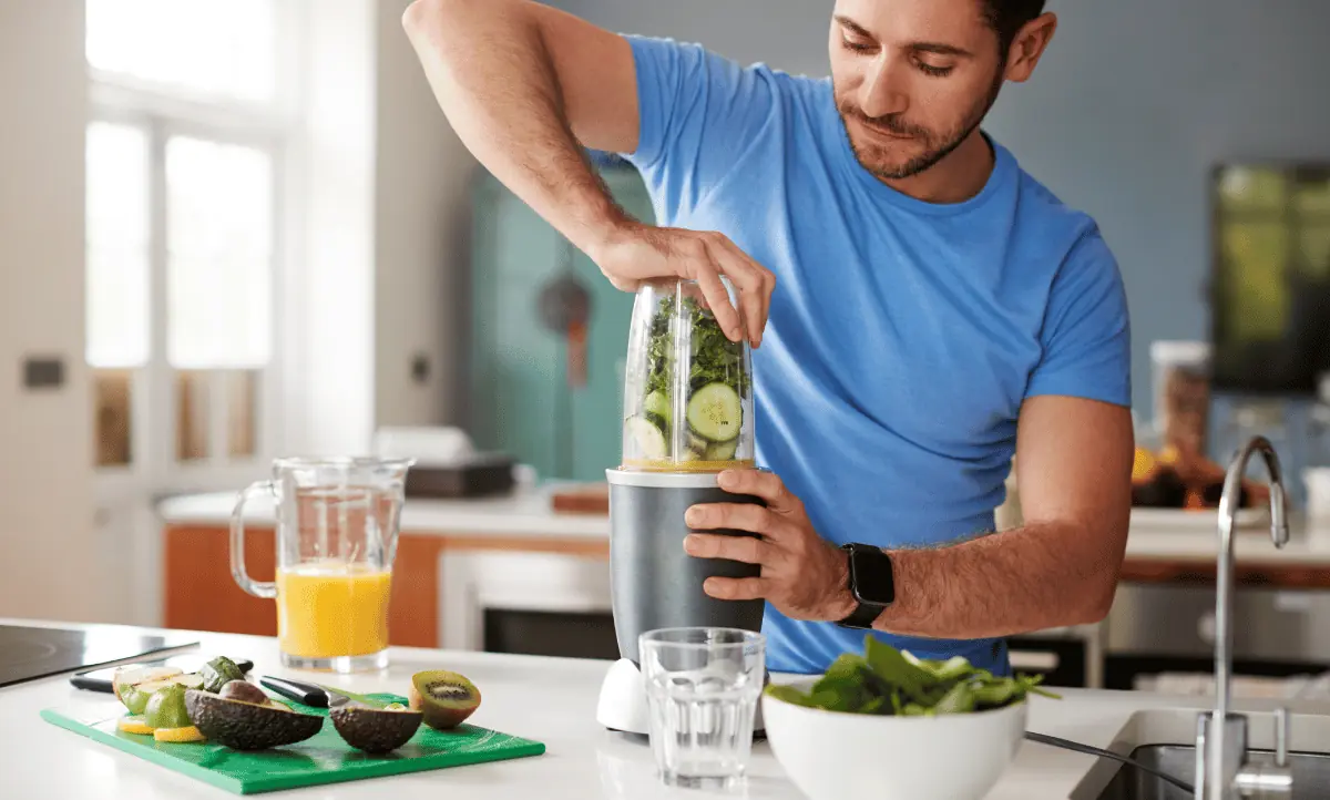 Een man bereidt een groene smoothie in de keuken, boordevol voedingsstoffen voor spieropbouw
