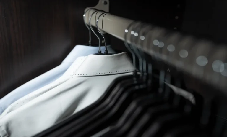 Witte en grijze overhemden hangen georganiseerd aan houten hangers in een stijlvolle kledingkast
