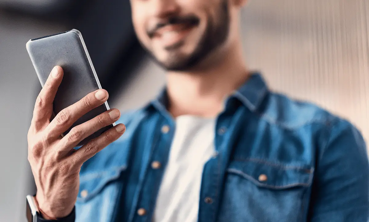 Een lachende man bekijkt zijn smartphone in close-up, een combinatie van technologie en lifestyle.