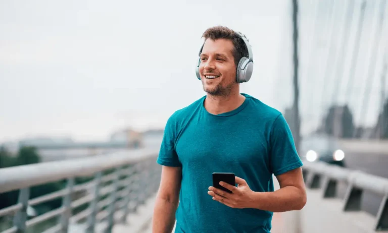 Man met een draadloze koptelefoon loopt over een brug terwijl hij lacht – testmoment voor de top 5 beste koptelefoons van 2025.|Sony WH-1000XM5 is een van de beste koptelefoons|de beste koptelefoon van 2025 nummer 5 Marshall Major IV koptelefoon|Skullcandy Crusher EVO koptelefoon|beste koptelefoon: Bose QuietComfort|draadloze koptelefoon voor op het werk JBL Tour One M2