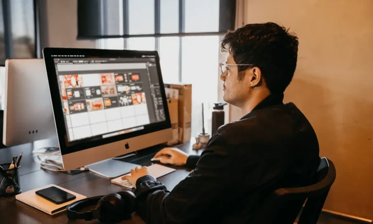 Een man werkt geconcentreerd achter een iMac-computer, met creatieve ontwerpen op het scherm, in een moderne werkomgeving.