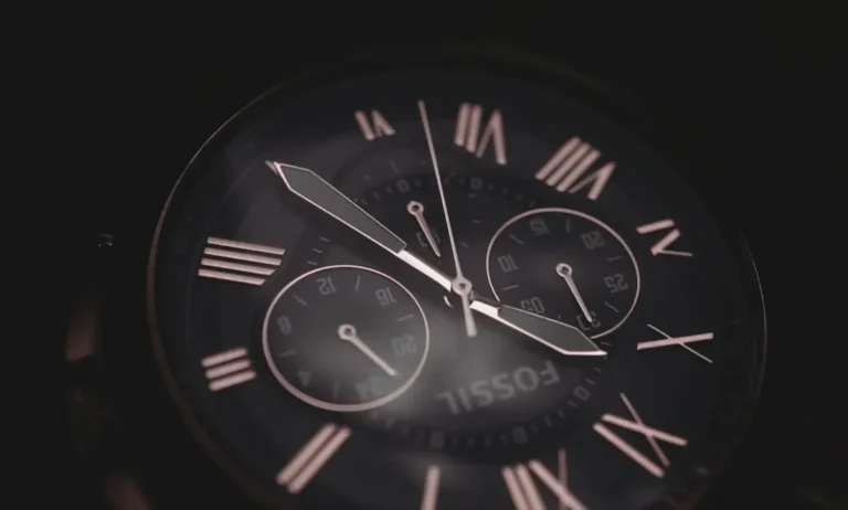 Een elegante close-up van een Fossil-horloge met een zwarte wijzerplaat en Romeinse cijfers, subtiel verlicht in een donkere setting.